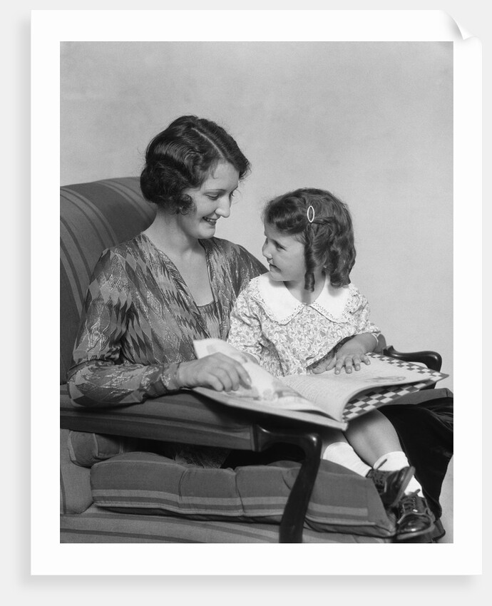 Mother & daughter smiling sitting in chair reading book by Anonymous
