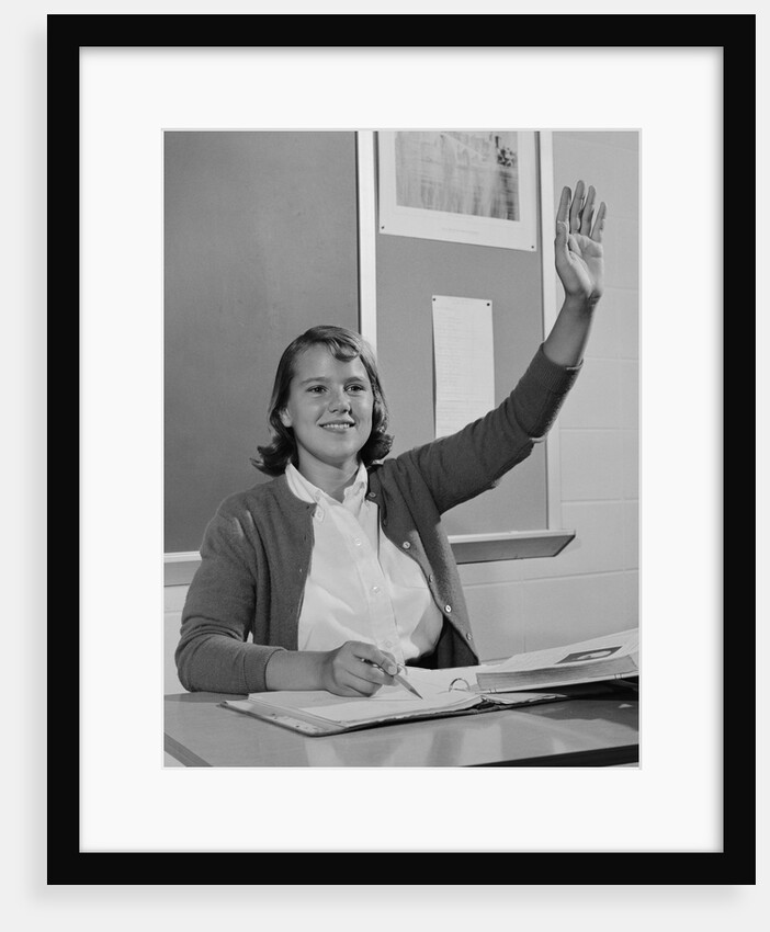 Smiling teen girl sitting classroom desk raising her hand by Anonymous