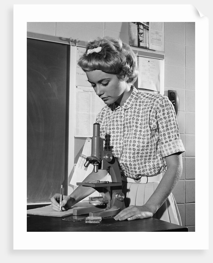 Teen girl writing notes working with microscope in science classroom by Anonymous