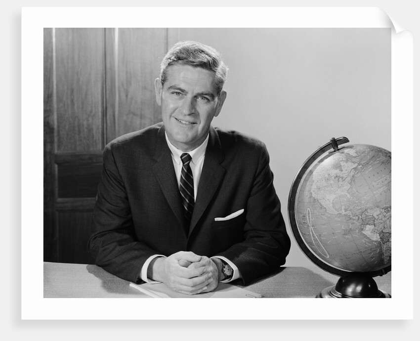 Smiling man sitting at desk with earth globe by Anonymous