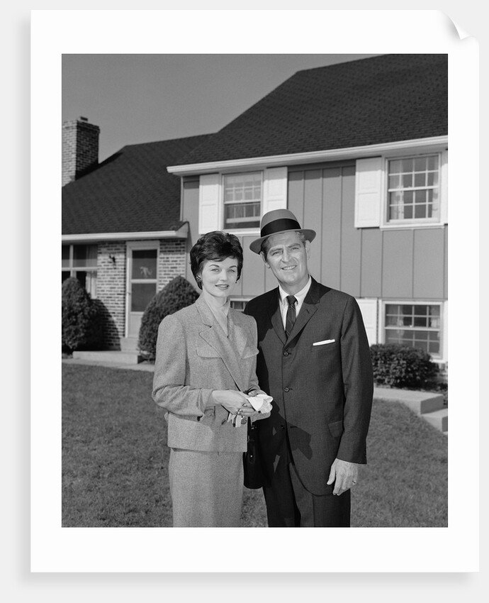 Couple smiling man and woman standing before suburban house by Anonymous