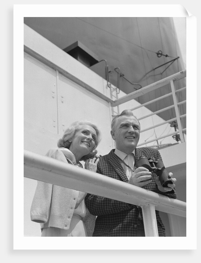 Smiling mature couple at shipboard rail with binoculars by Anonymous