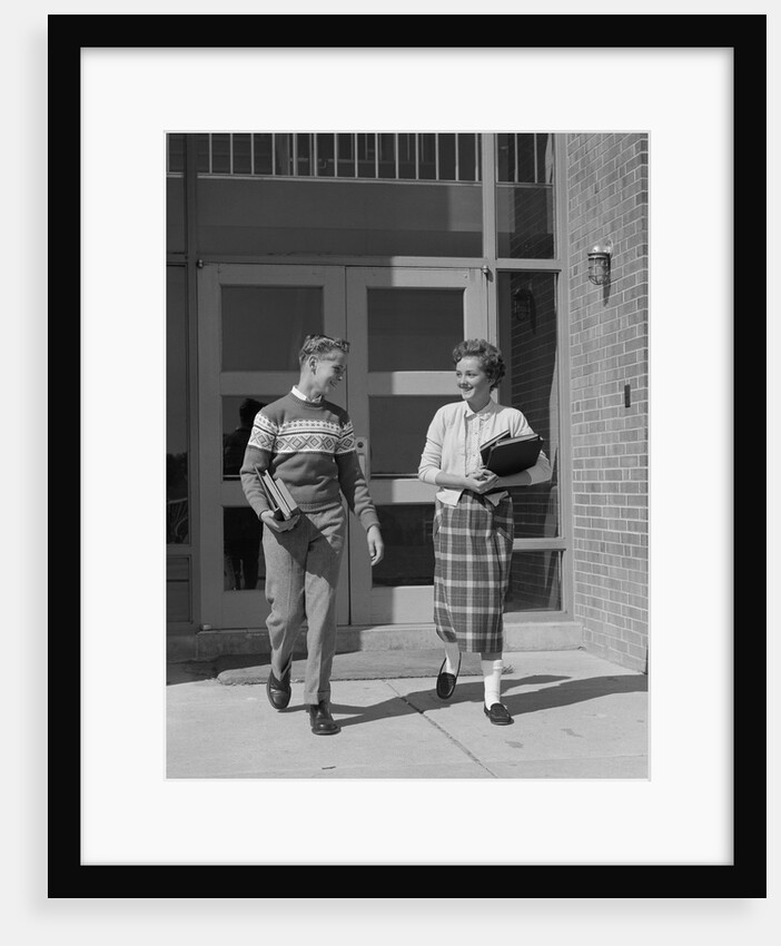 Two teenage students boy and girl walking away from school doors carrying books by Anonymous