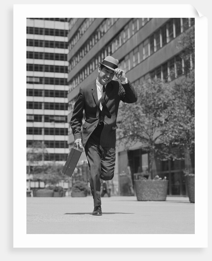 Businessman carrying briefcase holding his hat on running down urban sidewalk by Anonymous