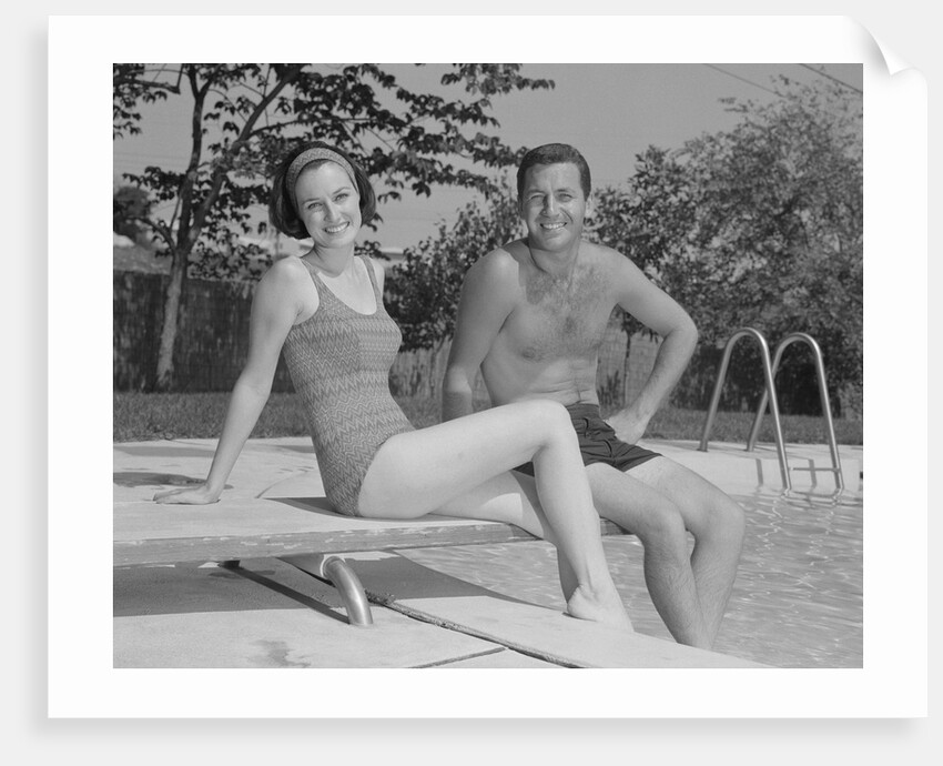 Man woman couple sitting on diving board on side of swimming pool by Anonymous