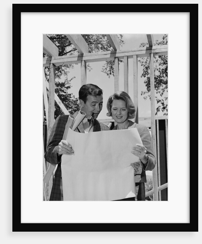 Couple looking at house plans blueprints man smoking pipe by Anonymous