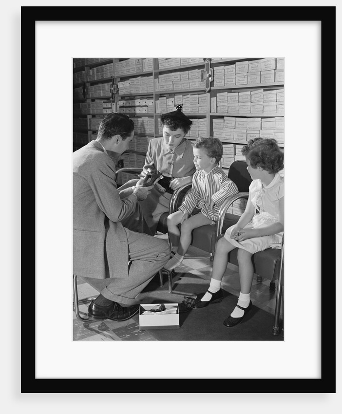 Family mother two children in shoe store trying new shoes helped by salesman by Anonymous