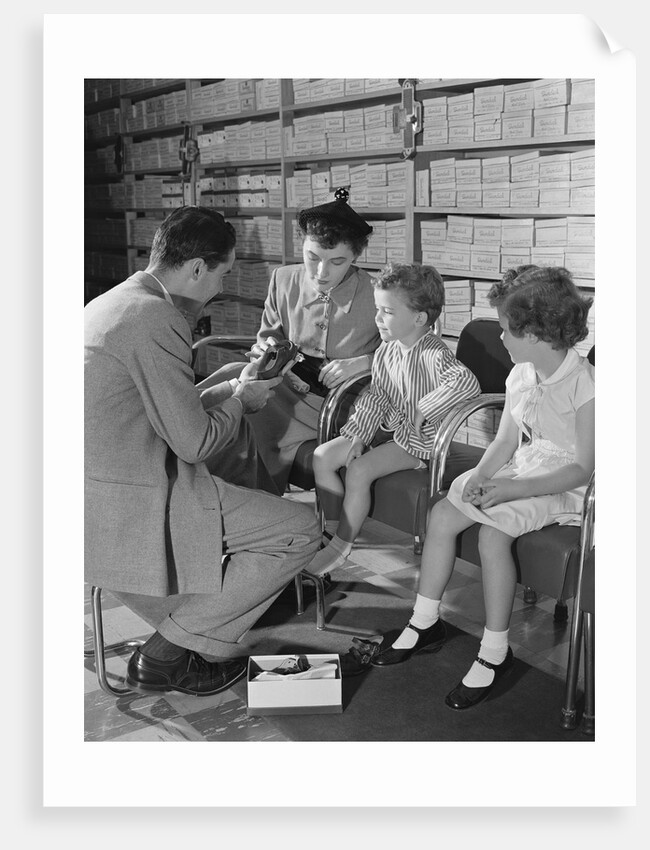 Family mother two children in shoe store trying new shoes helped by salesman by Anonymous