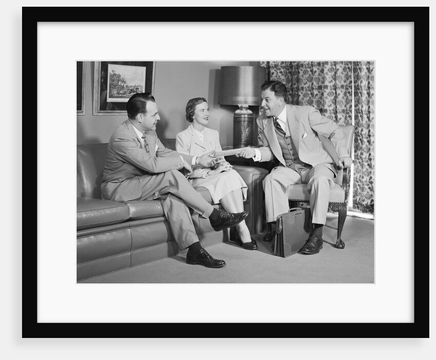 Couple sitting on couch talking to smiling insurance salesman handing them a policy by Anonymous