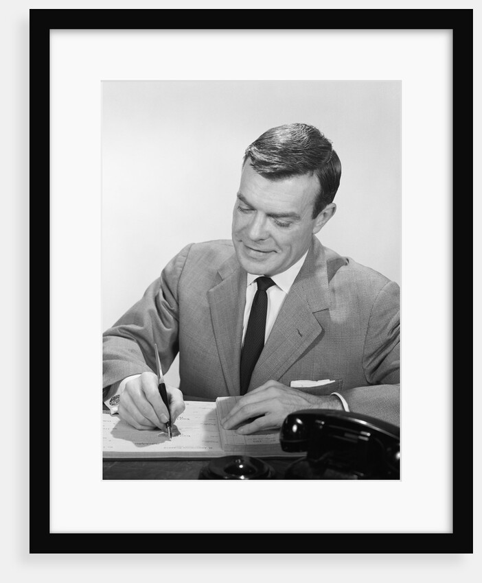 Smiling businessman at desk writing checks by Anonymous
