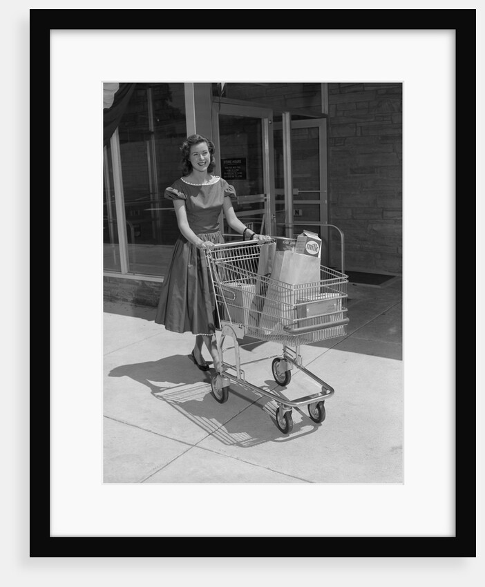 Smiling woman pushing grocery cart out of supermarket by Anonymous