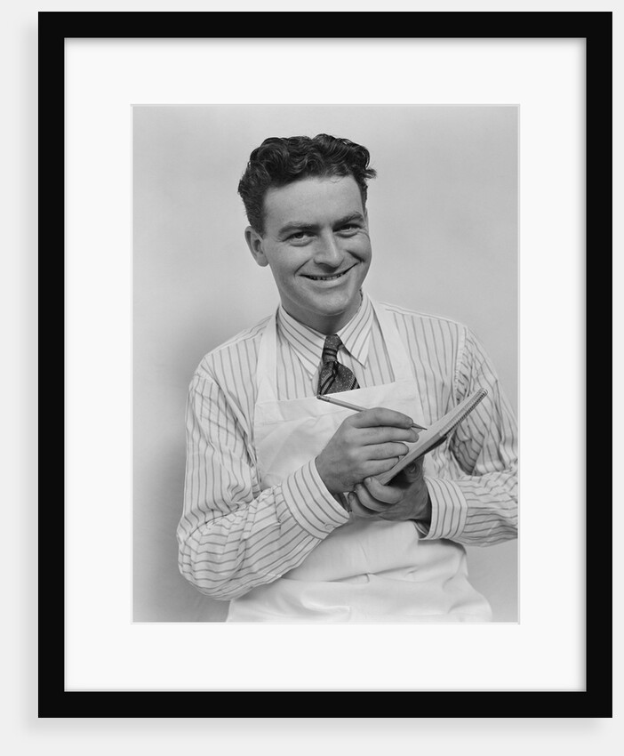 Smiling curly hair man wearing apron taking order with pencil and note pad by Anonymous