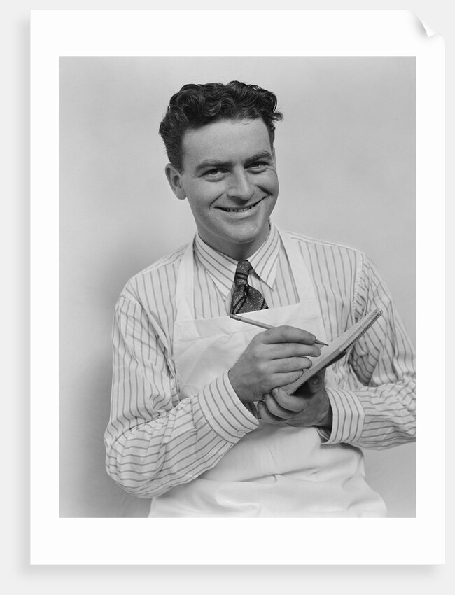 Smiling curly hair man wearing apron taking order with pencil and note pad by Anonymous