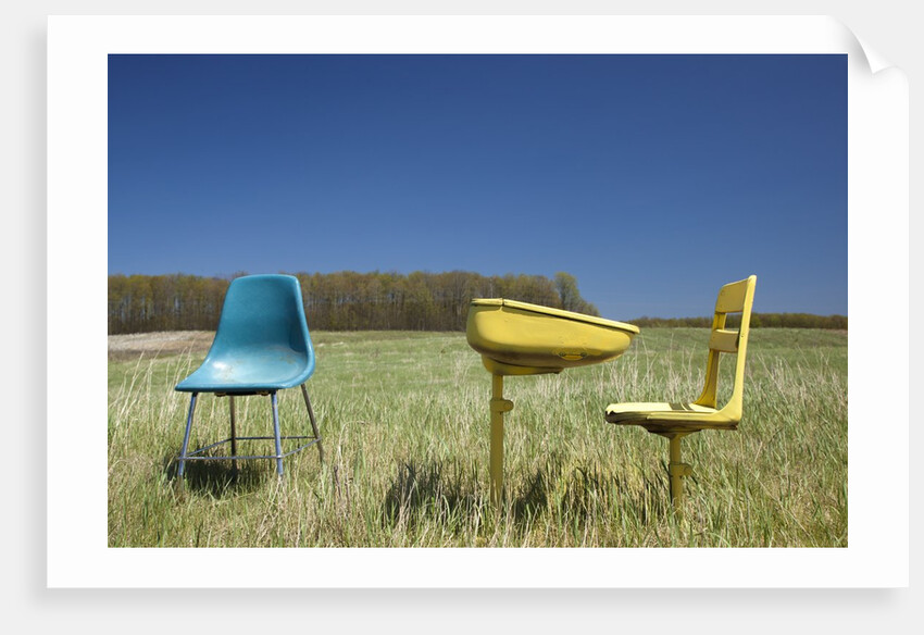 Abandoned school desk anc chairs in field by Anonymous