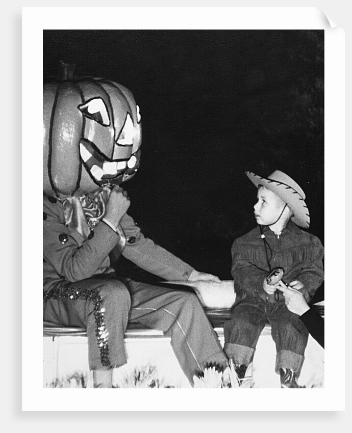 Young boy warily eyes pumpkin man, ca. 1955 by Corbis