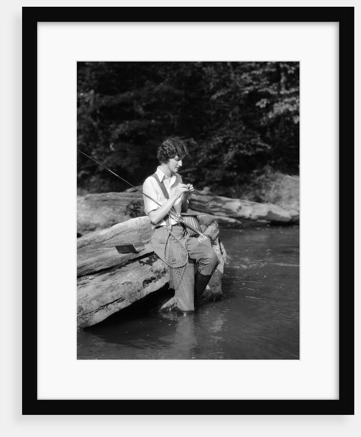 1920s 1930s woman sitting on rock by side of stream wearing waders putting fly on tippet by Anonymous