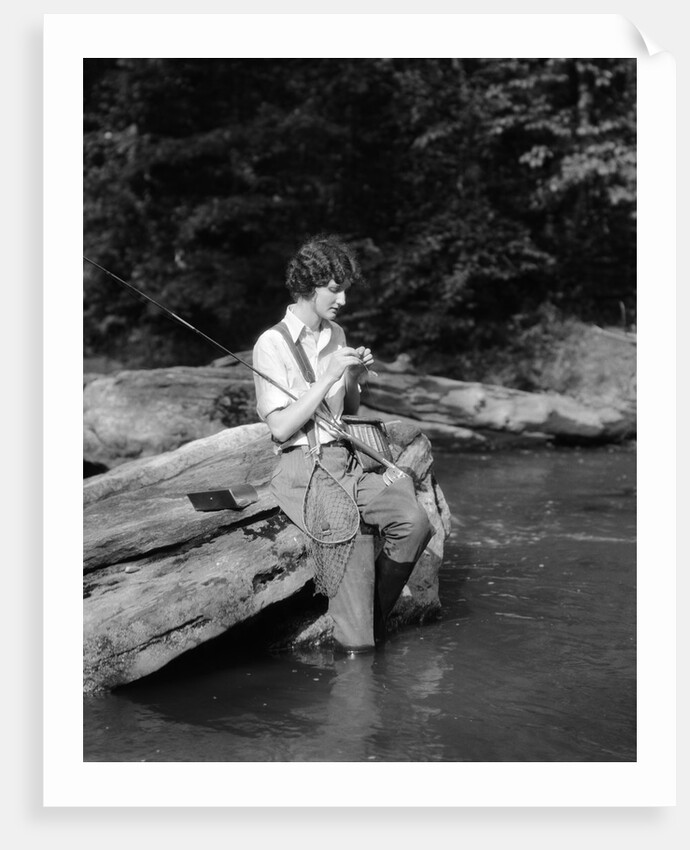 1920s 1930s woman sitting on rock by side of stream wearing waders putting fly on tippet by Anonymous