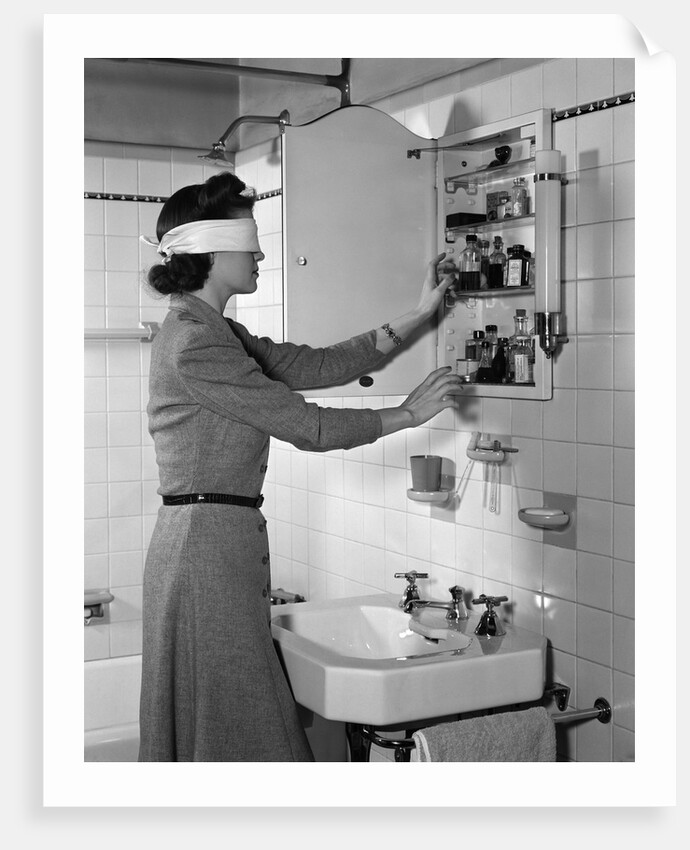 1940s woman wearing blindfold reaching into bathroom medicine cabinet by Anonymous