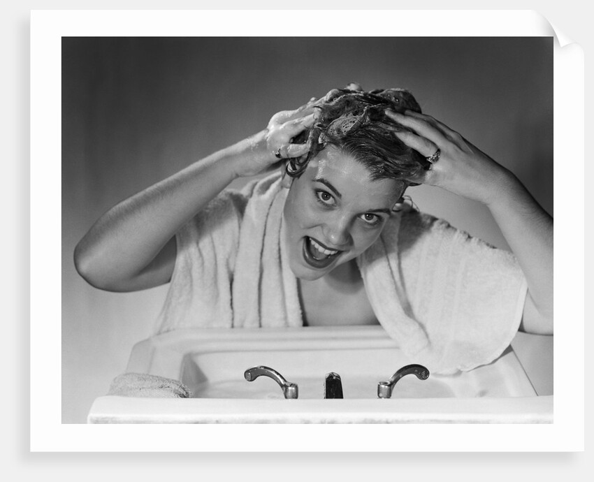 1950s smiling woman washing shampooing hair in sink looking at camera by Anonymous