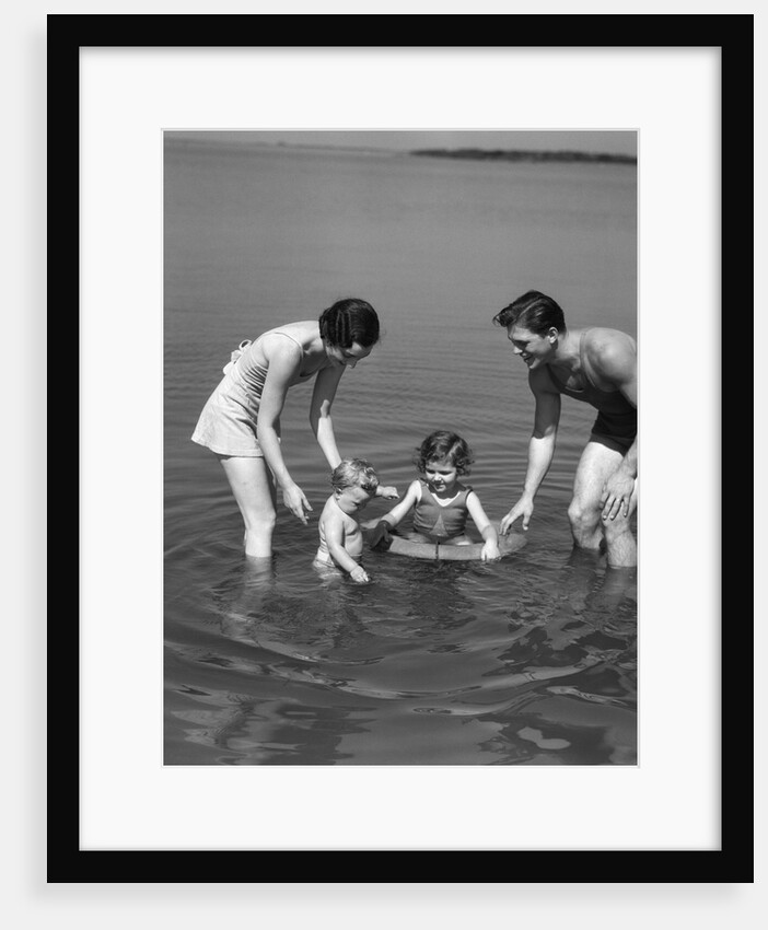 1930s family father mother daughter son with rubber inner tube wading in seashore water by Anonymous
