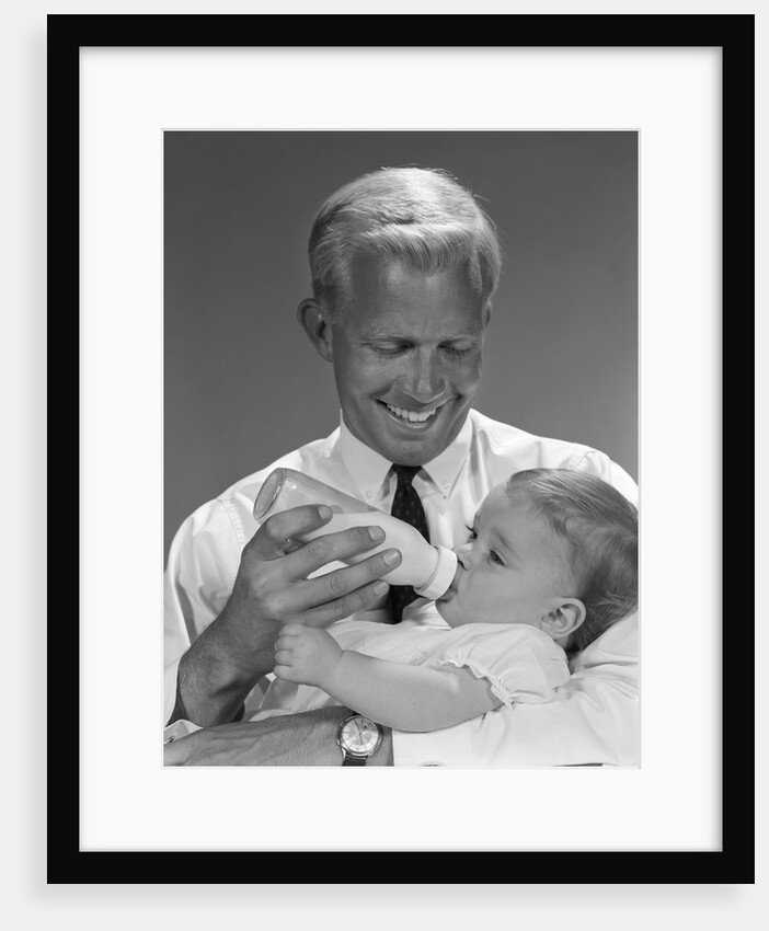 1960s smiling blond father feeding child milk in glass baby bottle by Anonymous