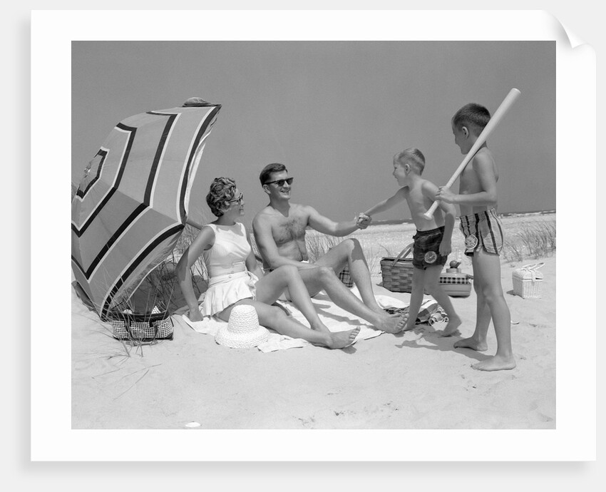1960s at the beach two boys with baseball bat trying to pull up father seated next to mother so he will play with them by Anonymous