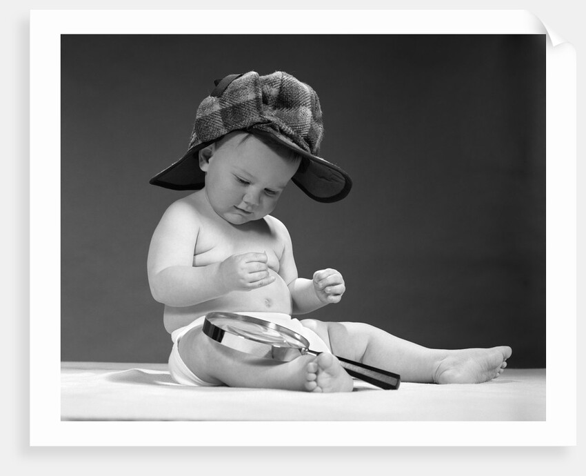1960s baby in diaper wearing sherlock holmes deerstalker style double-billed cap with magnifying glass resting on leg inspecting a clue by Anonymous