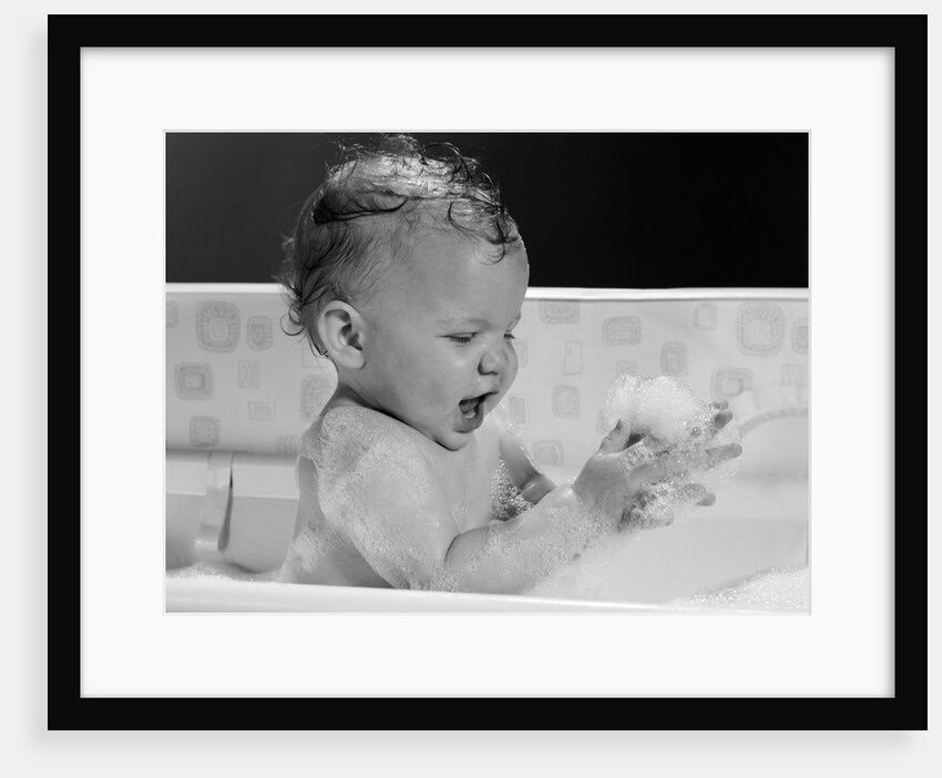 1960s baby in bathtub playing with suds indoor by Anonymous