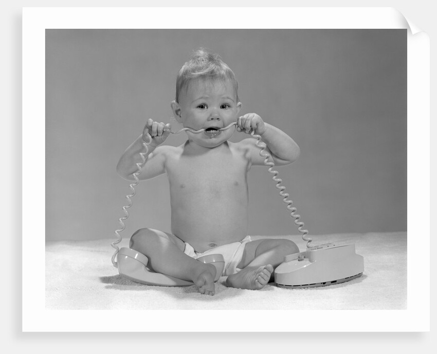 1960s blond baby sitting up looking at camera chewing on telephone cord by Anonymous
