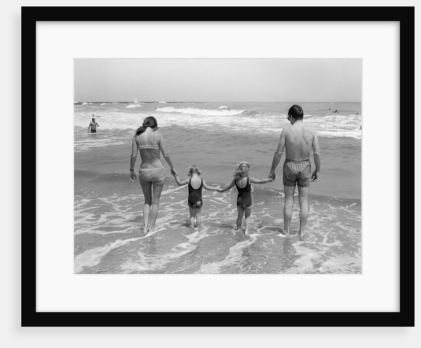 1970s family on vacation at ocean beach holding hands walking on sand in surf by Anonymous