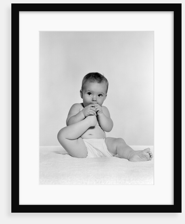 1950s 1960s baby seated on blanket bringing foot to mouth by Anonymous