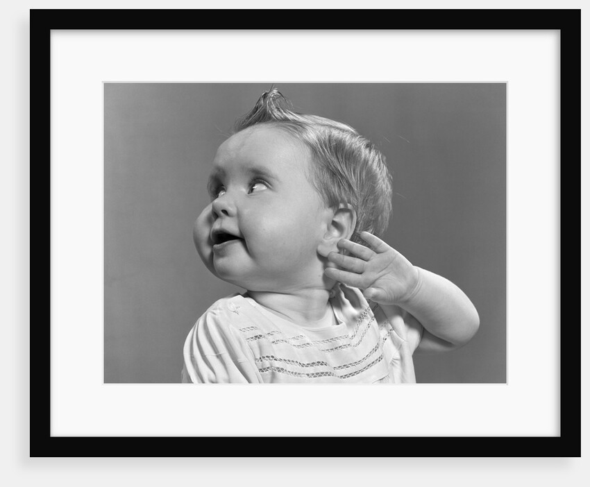 1940s 1950s close-up portrait of baby girl with curl on top of head looking to side with hand held up beside ear by Anonymous