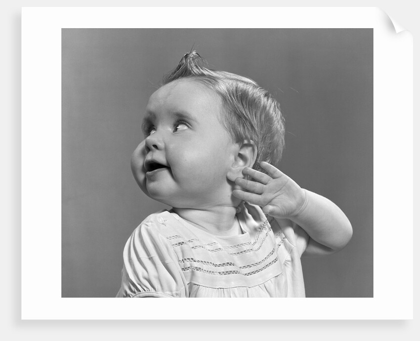 1940s 1950s close-up portrait of baby girl with curl on top of head looking to side with hand held up beside ear by Anonymous