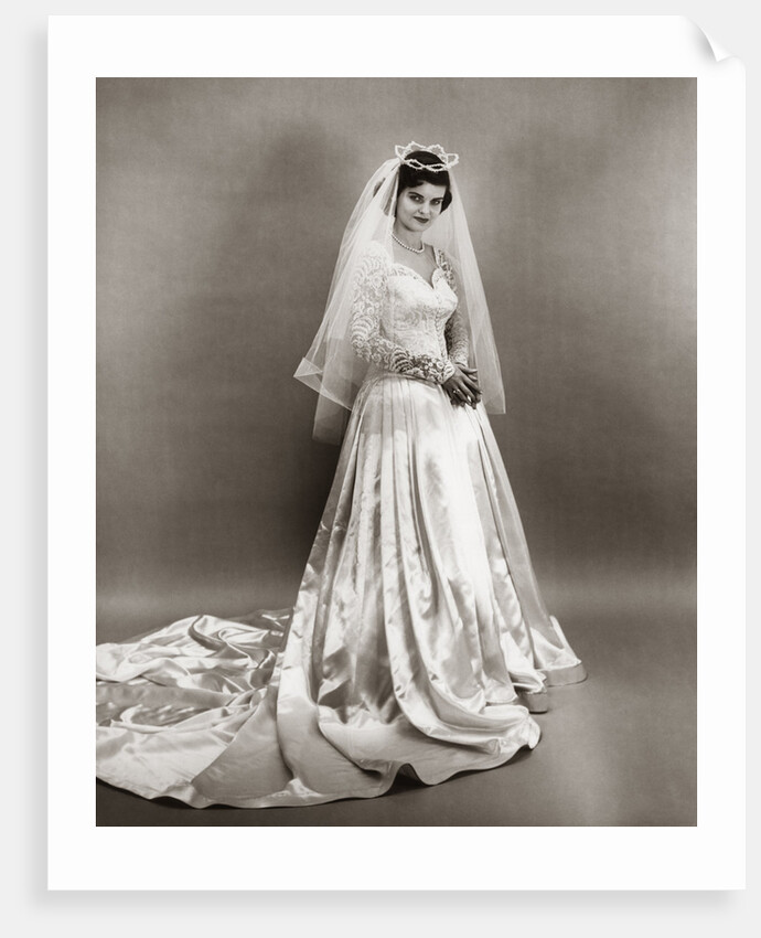 1950s full length portrait bride standing wearing satin and lace wedding gown veil and tiara looking at camera by Anonymous