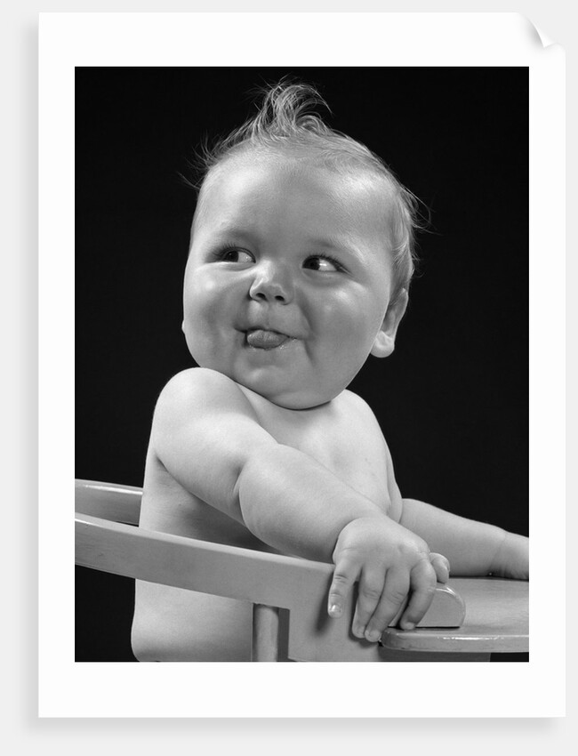1950s 1940s baby in high chair head turned to one side with tongue sticking out funny facial expression by Anonymous