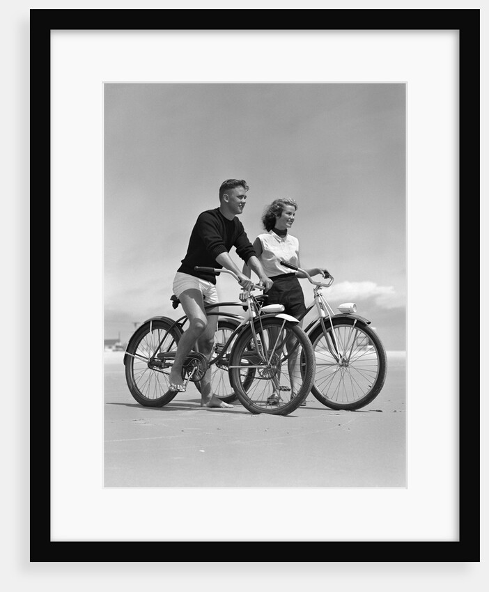 1950s teenage boy and girl with bikes on the beach by Anonymous