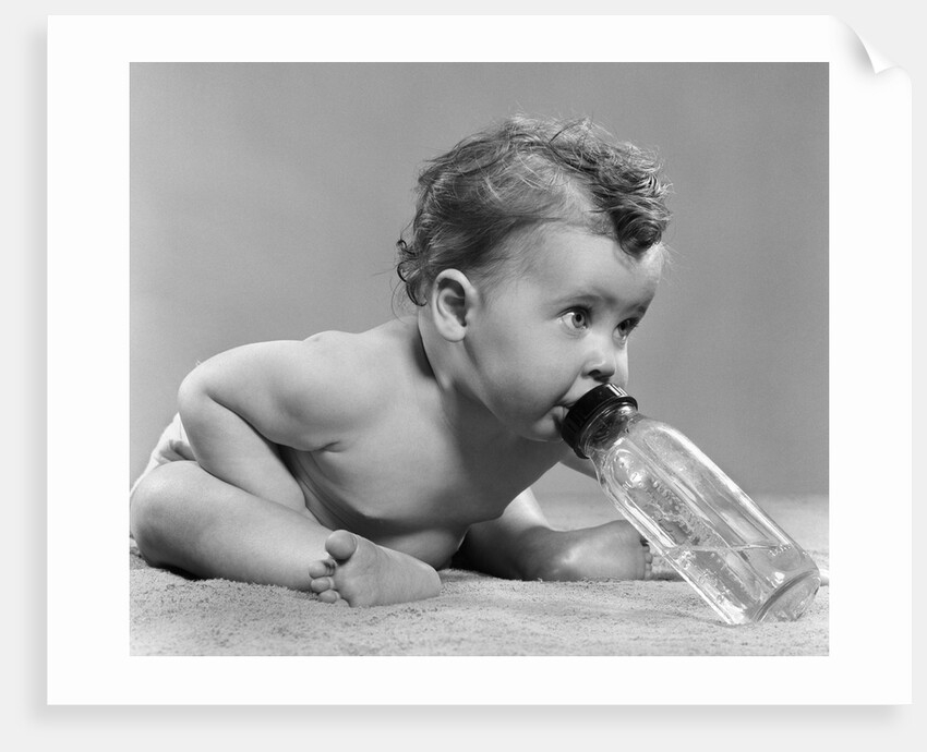 1950s baby sitting leaning forward drinking from bottle studio indoor by Anonymous