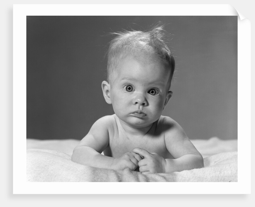1960s portrait baby lying on stomach with messy hair and bulging eyes looking at camera by Anonymous