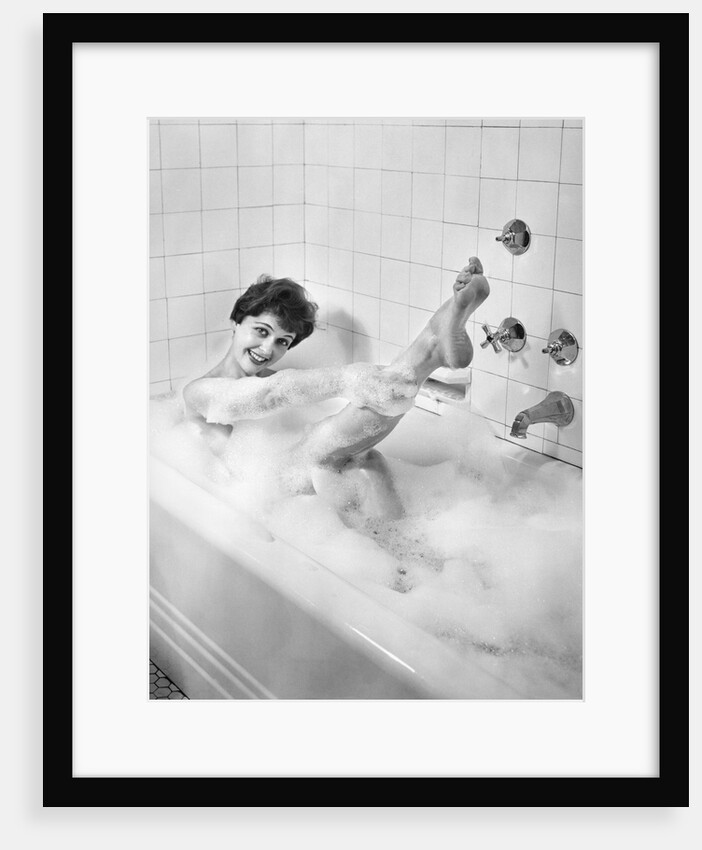 1950s sexy smiling woman taking a soap suds bubble bath in tub looking at camera by Anonymous