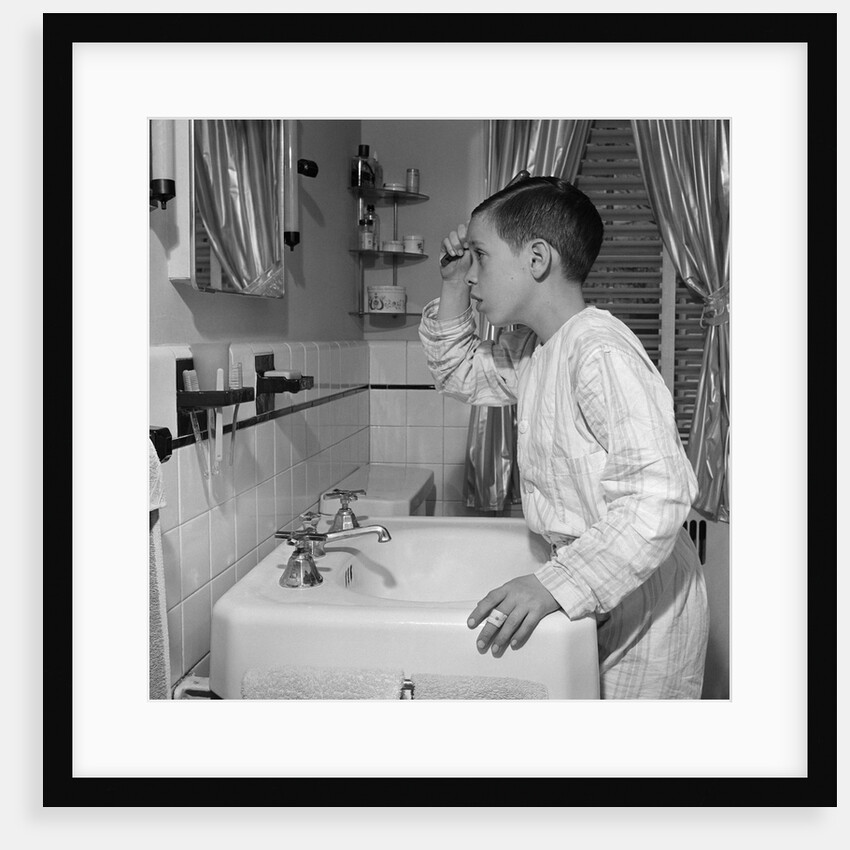 1950s boy combing hair looking in bathroom sink mirror by Anonymous