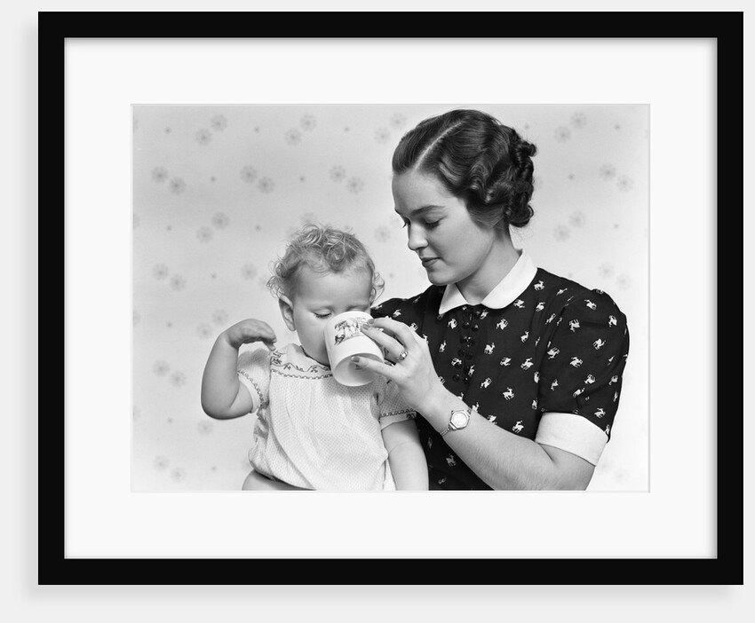 1930s woman mother giving baby daughter drink from mug by Anonymous