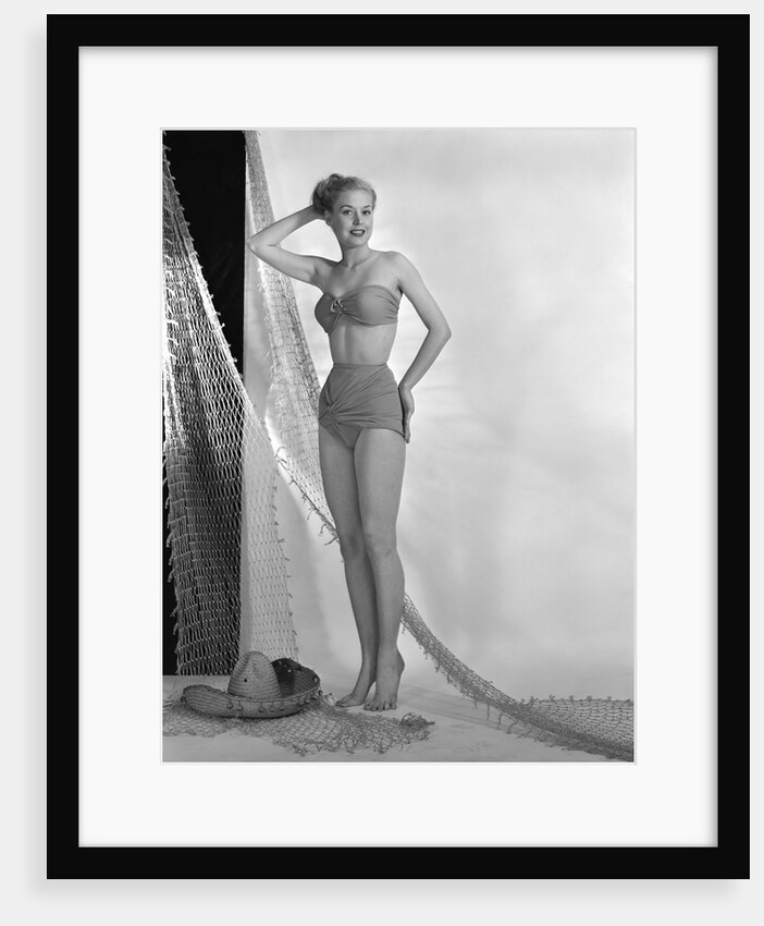 1950s glamour girl looking at camera posed in studio draped in fishing net wearing two piece bathing suit by Anonymous