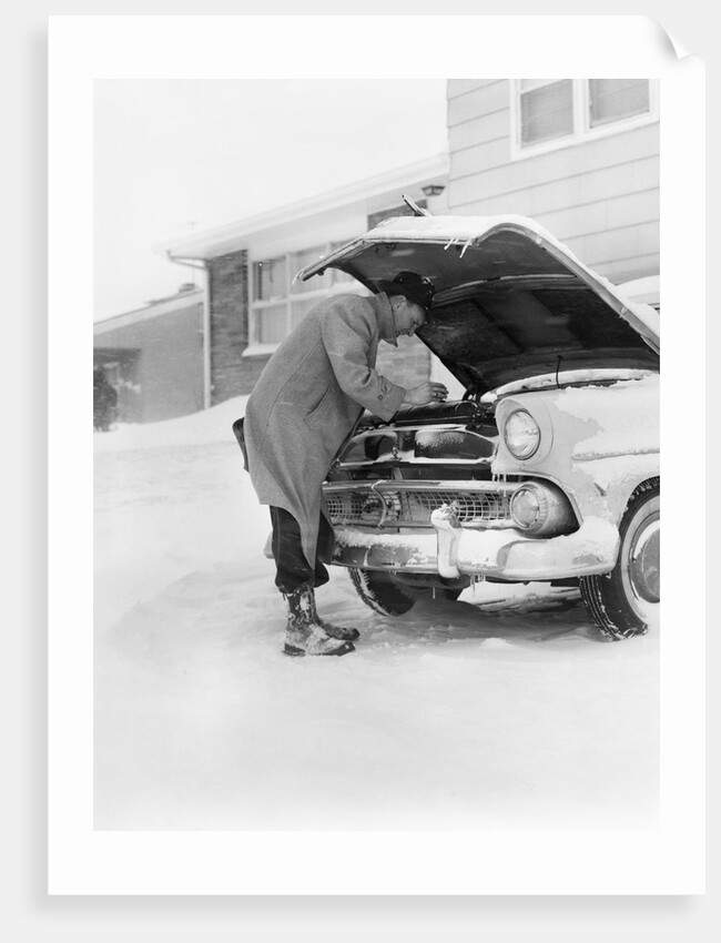 1950s man winter driveway trying to start fix car hood up by Anonymous