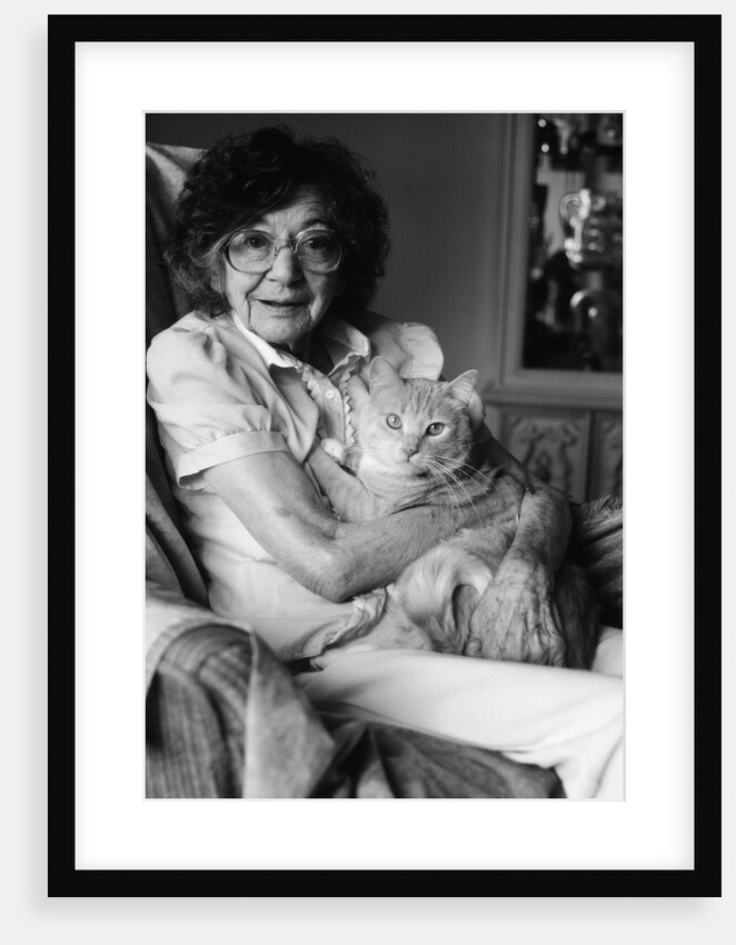 1980s elderly senior woman wear glasses holding tabby cat in her arms lap pet geriatric companion old age therapy animal looking at camera by Anonymous