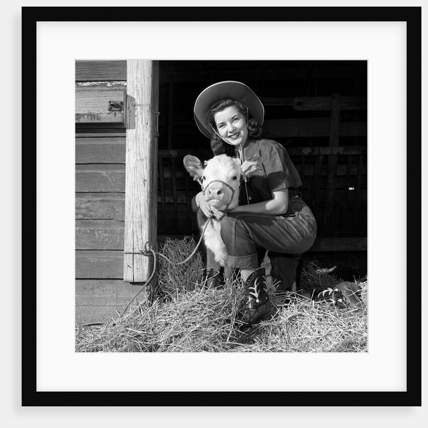 Girl posing with calf in straw filled stall in barn by Anonymous