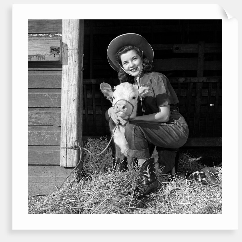 Girl posing with calf in straw filled stall in barn by Anonymous