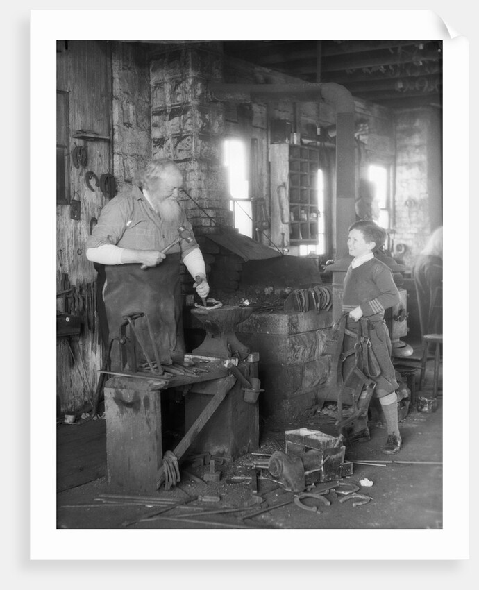 1930s elderly blacksmith with hammer at anvil as young boy holding harness looks on smiling by Anonymous