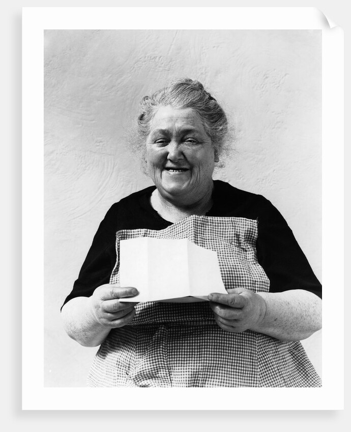 1930s 1940s elderly character woman smiling reading letter wearing apron looking at camera by Anonymous