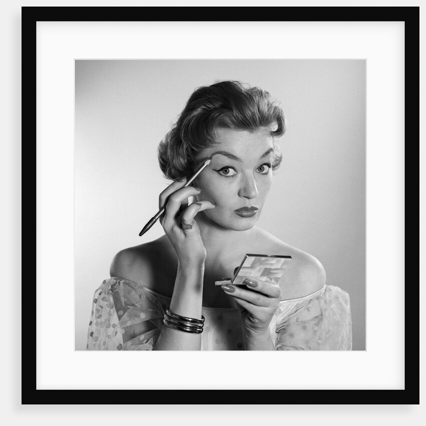 1950s 1960s woman looking at camera applying makeup eye brow pencil holding compact mirror by Anonymous