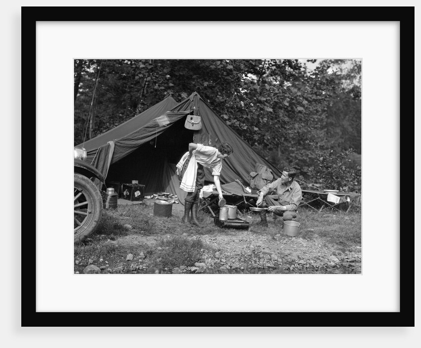1920s couple man woman on fishing camping trip vacation at campsite man cooking over fire by Anonymous
